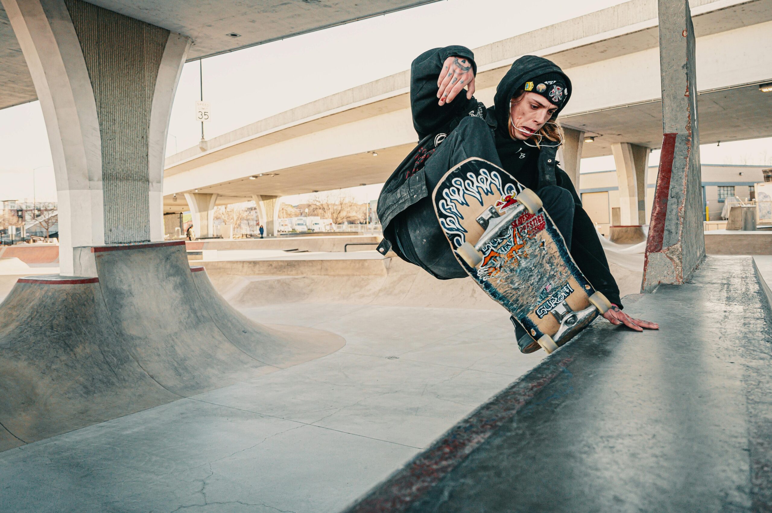 A skateboarder executing a stylish trick in an urban skate park under a bridge.