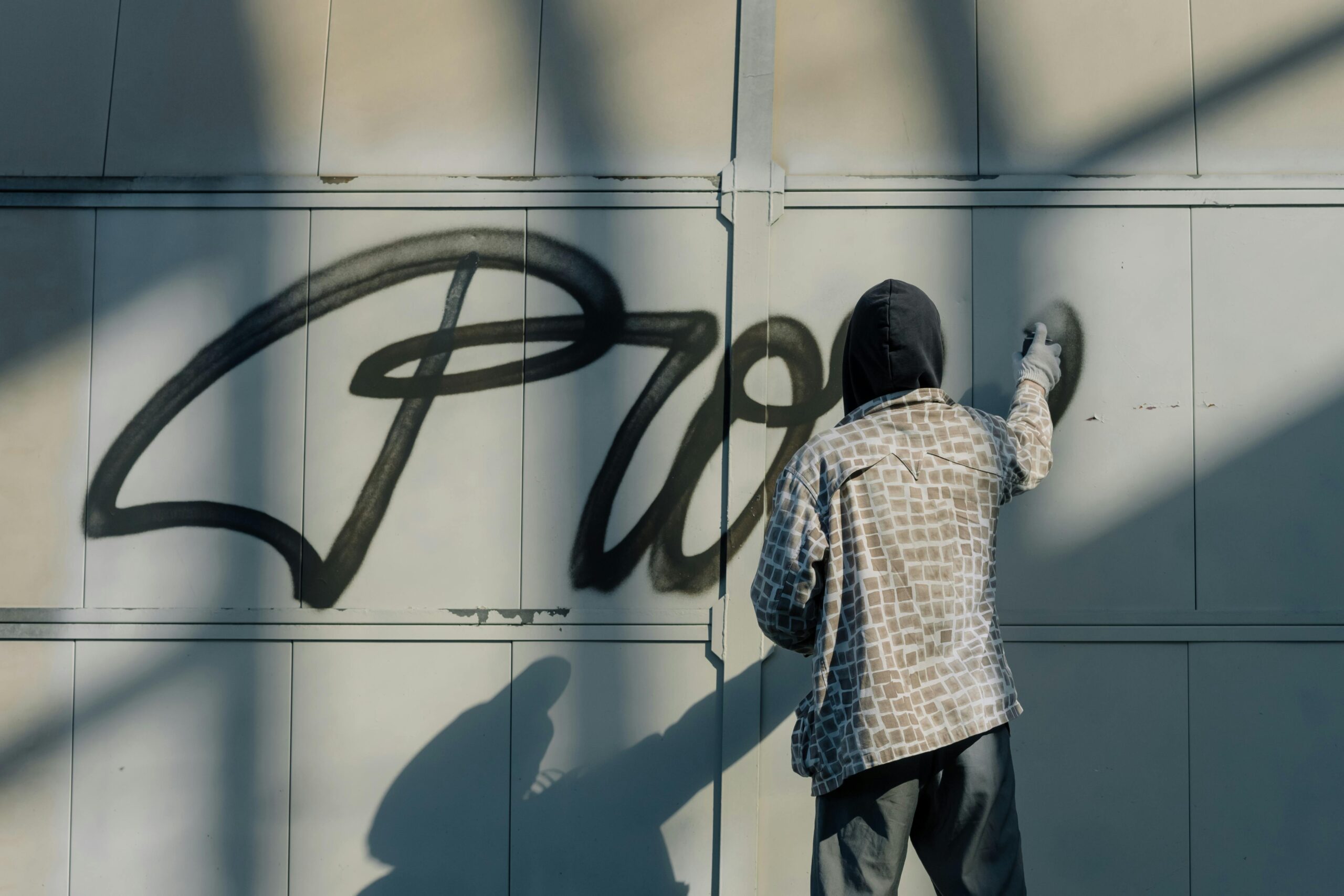 A street artist spray painting graffiti art on a wall, with shadows creating a dramatic light effect.